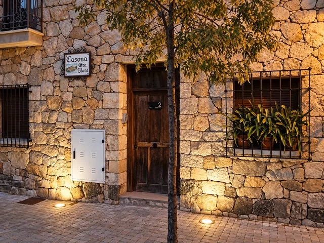 Detalle de puerta, ventana y piedra de fachada con iluminación desde el suelo.