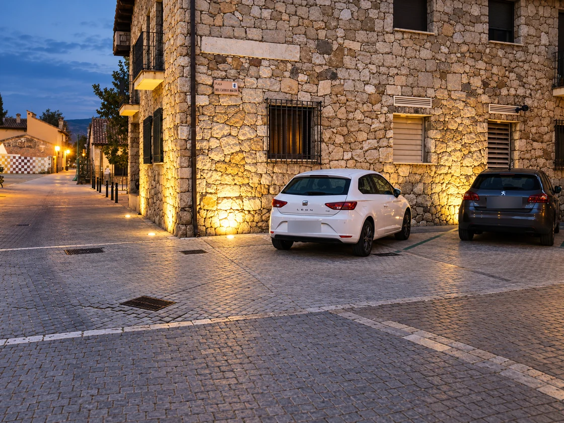 Fachada de piedra iluminada desde el pavimento, junto a la zona de aparcamiento.