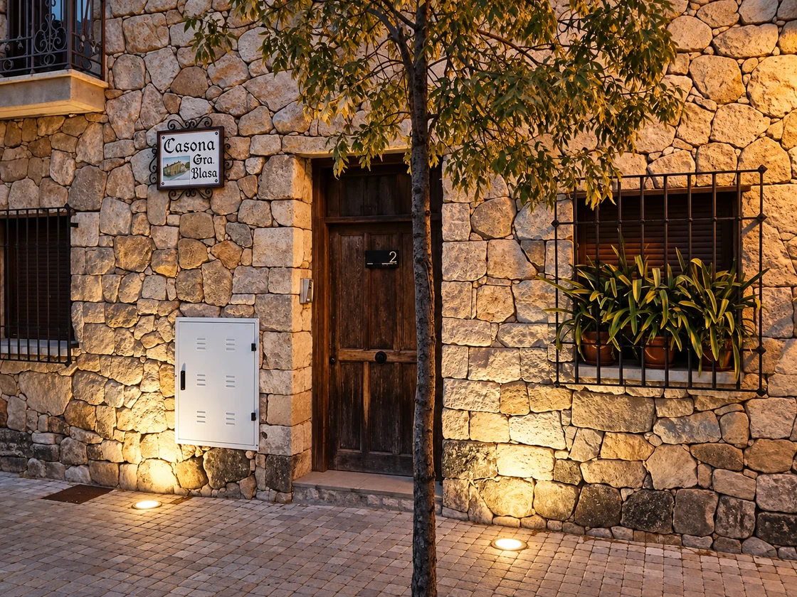 Detalle de puerta, ventana y piedra de fachada con iluminación desde el suelo.